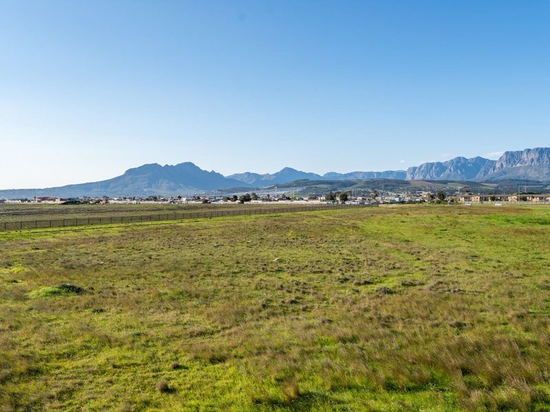 A wide-angle view of the surrounding landscape featuring open fields and distant mountain ranges under a clear blue sky.