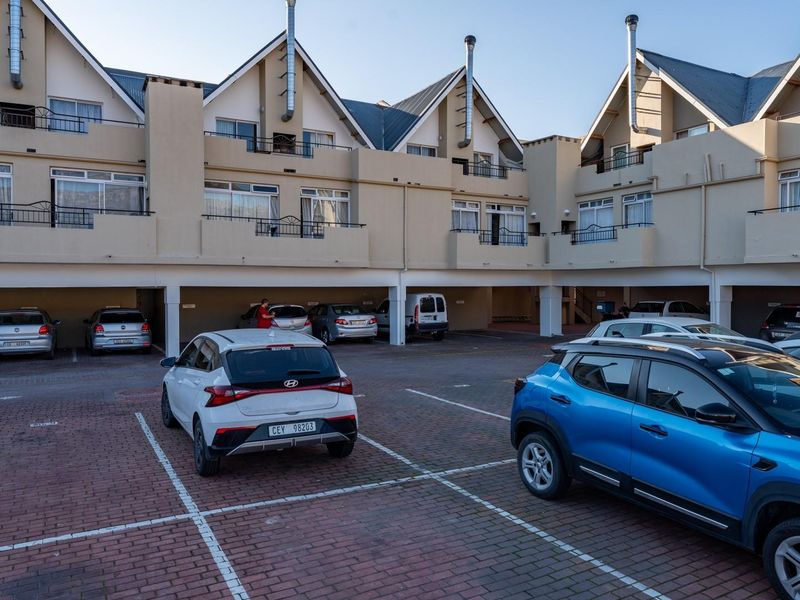 Exterior view of an apartment complex featuring covered ground-level parking bays and upper-level balconies with chimney flues.