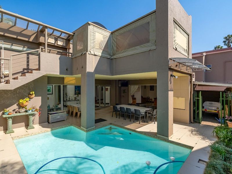 A spacious outdoor entertainment area featuring a swimming pool, covered patio with dining space, and an external staircase leading to an upper level.