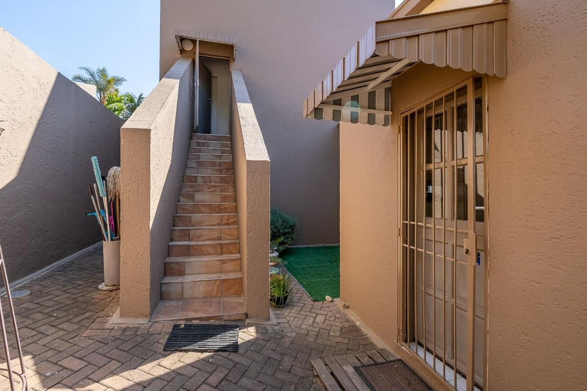 A rear courtyard area featuring a paved surface, an external staircase leading to an upper level, and a secure entrance with a metal gate.