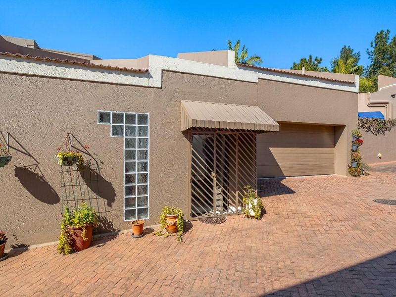 Front exterior view of the property featuring a brick paved driveway, integrated garage, and secure entrance with a protective awning.