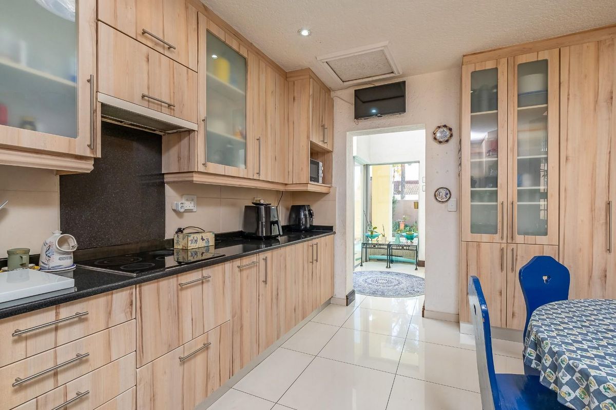 A functional kitchen featuring light-wood cabinetry, black granite countertops, an electric hob, and tiled flooring, with direct access to an outdoor patio area.