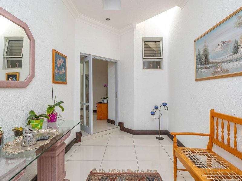 A bright entrance hall featuring tiled flooring, coving, and a glass panel door leading to an adjacent room.