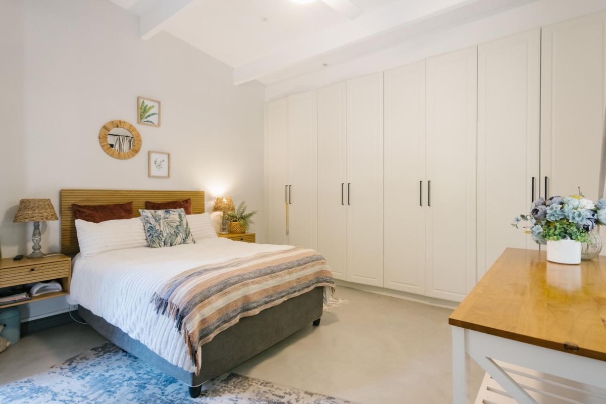 A well-maintained bedroom featuring extensive built-in wardrobes, polished concrete flooring, and exposed ceiling beams, offering a clean and modern aesthetic.