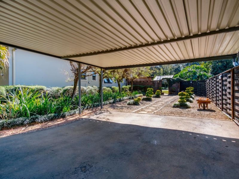 A well-maintained covered carport area featuring a corrugated metal roof, concrete driveway, and adjacent landscaped garden beds.