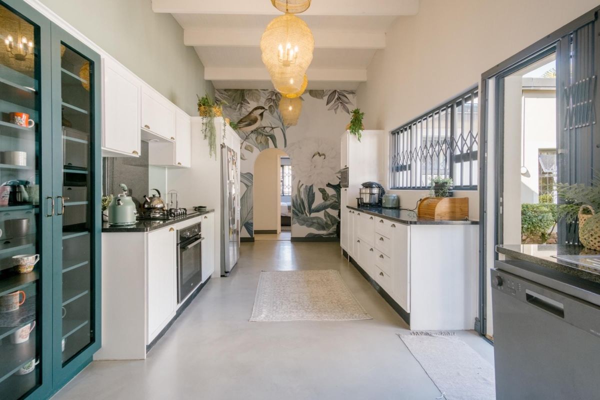 Modern galley-style kitchen featuring white cabinetry, dark stone countertops, built-in appliances, exposed ceiling beams, and a decorative floral feature wall.