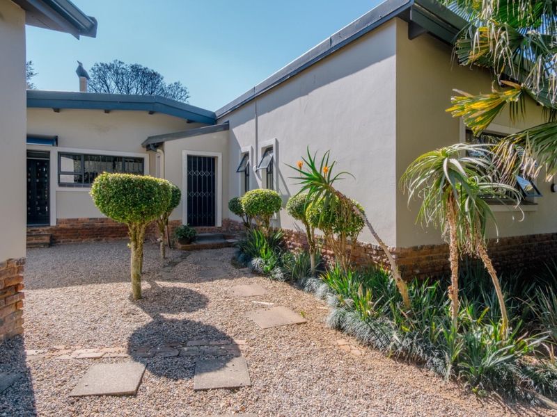A well-maintained rear courtyard featuring a gravel surface, paved walkway, and established landscaping against the exterior brick and plaster wall of the house.