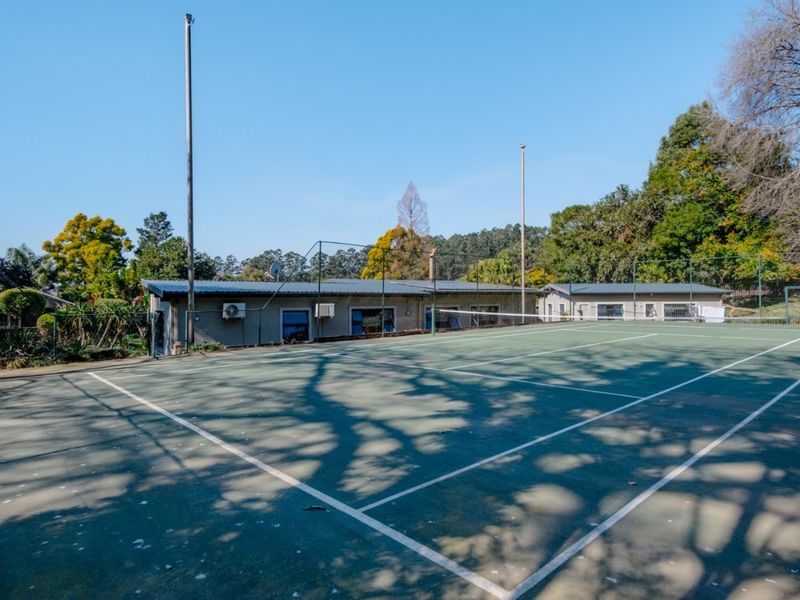 A private tennis court with perimeter fencing and floodlight poles, situated adjacent to the main residential building.