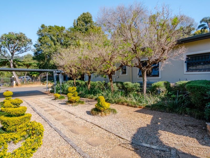 Front exterior view of the property featuring a gravel driveway, a carport, and a well-maintained landscaped garden with a paved walkway.