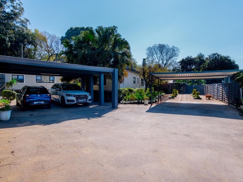 Spacious front exterior featuring a double carport, additional single carport, paved driveway, and well-maintained landscaped garden area.