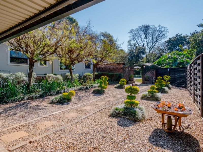 A well-maintained garden featuring gravel landscaping, stone pathways, and established topiary shrubs, viewed from under a covered patio area.