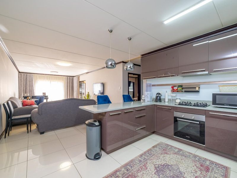 Modern open-plan living area featuring a sleek kitchen with glossy cabinetry, stone countertops, and integrated appliances, flowing into a comfortable lounge space.