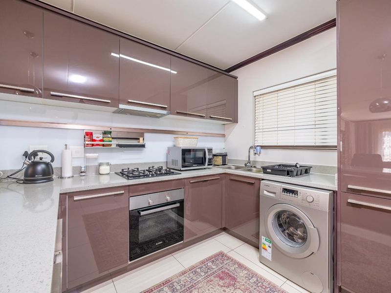 Modern kitchen featuring high-gloss cabinetry, stone countertops, built-in gas hob, electric oven, and integrated laundry facilities.