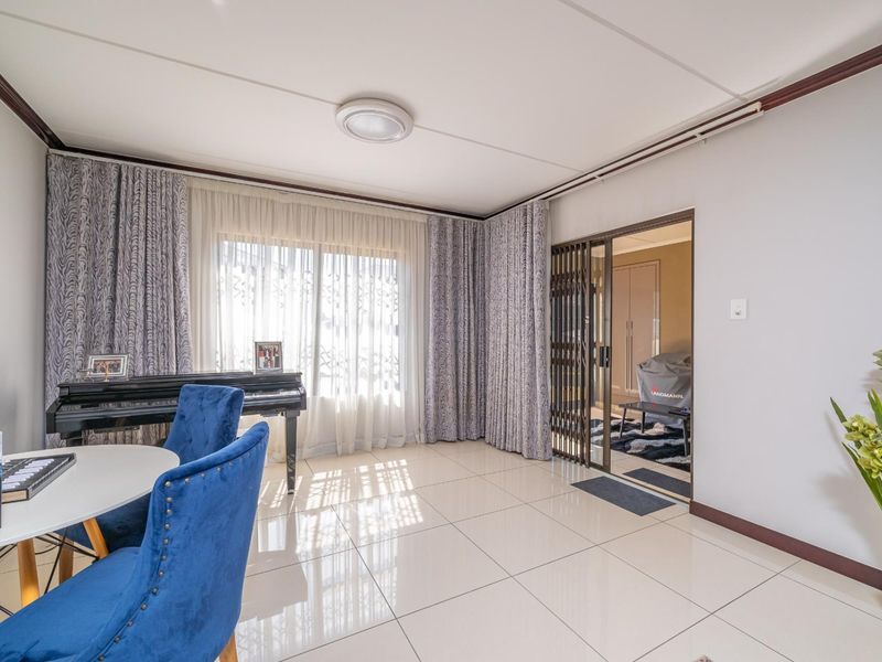 A bright living area featuring large windows with curtain tracks, polished tiled flooring, and a sliding glass door leading to an adjacent room.