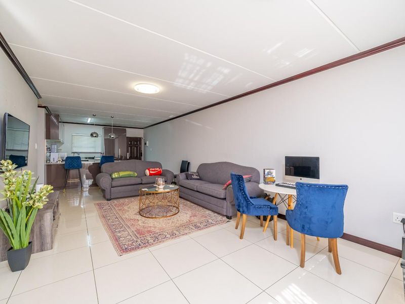 An open-plan living and kitchen area featuring neutral tiled flooring, modern cabinetry, and a spacious layout suitable for comfortable apartment living.