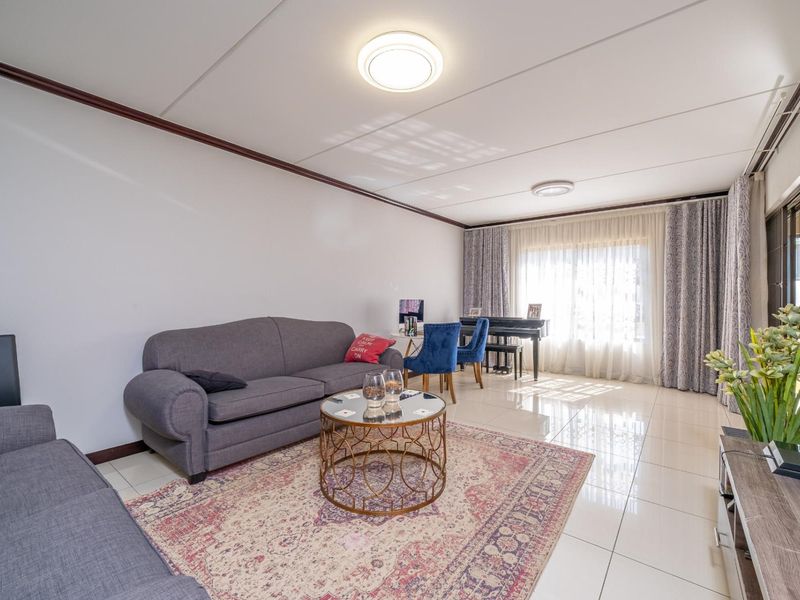 A bright and spacious living room featuring polished tile flooring, neutral walls, and large windows with curtains allowing for ample natural light.