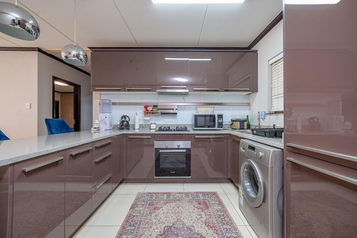 Modern kitchen featuring high-gloss cabinetry, stone countertops, built-in oven, gas hob, and integrated laundry facilities with tiled flooring.