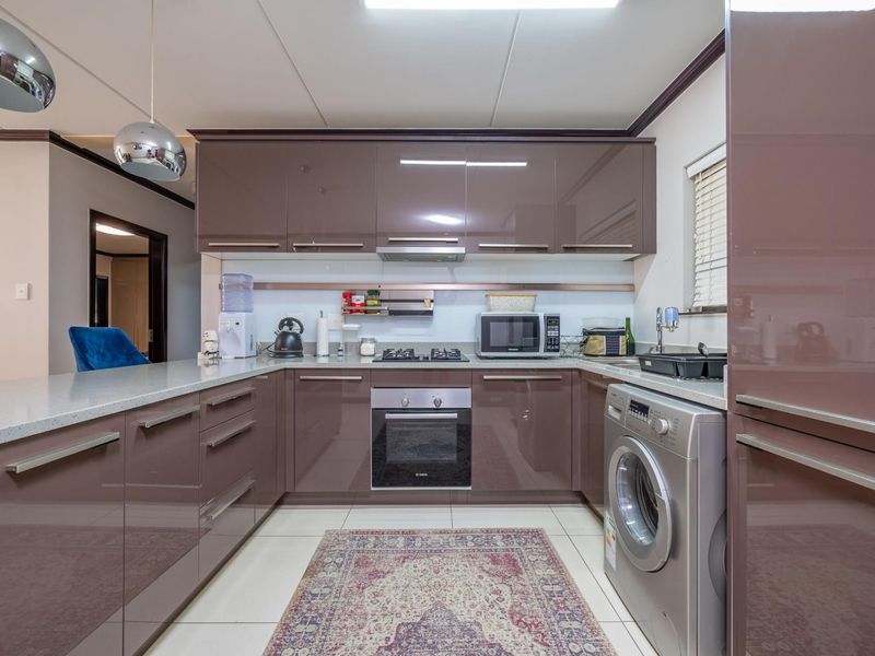 Modern kitchen featuring high-gloss cabinetry, stone countertops, built-in oven, gas hob, and integrated laundry facilities with tiled flooring.