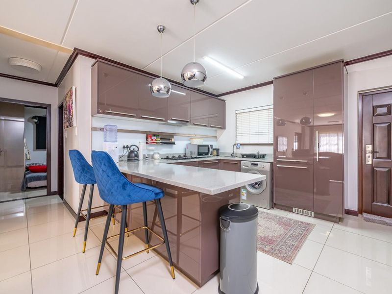 Modern kitchen featuring high-gloss cabinetry, stone countertops, a breakfast bar, and integrated appliances, finished with sleek tiled flooring and contemporary pendant lighting.