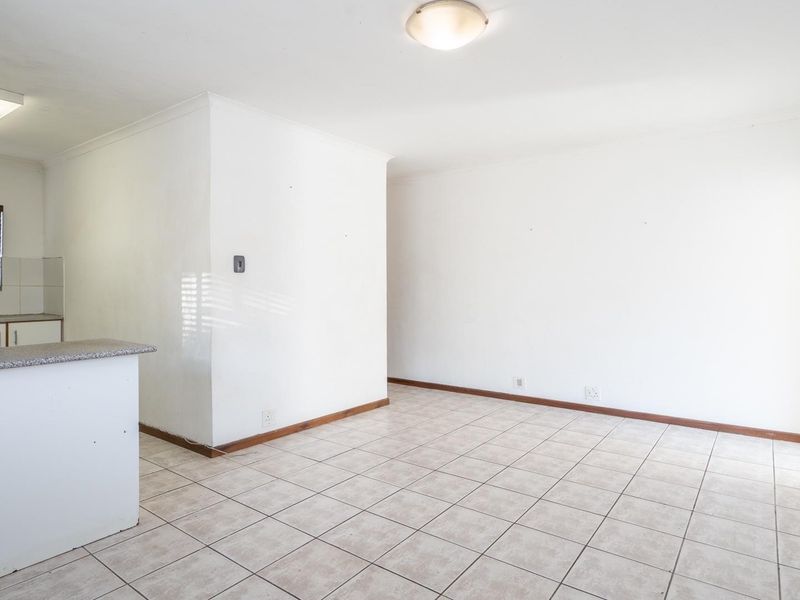An open-plan living and kitchen area featuring tiled flooring, neutral walls, and a functional kitchen layout with granite countertops.