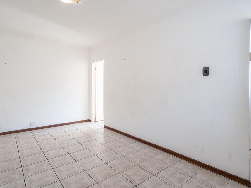 An empty, neutrally painted living area featuring tiled flooring and direct access to an exterior door.