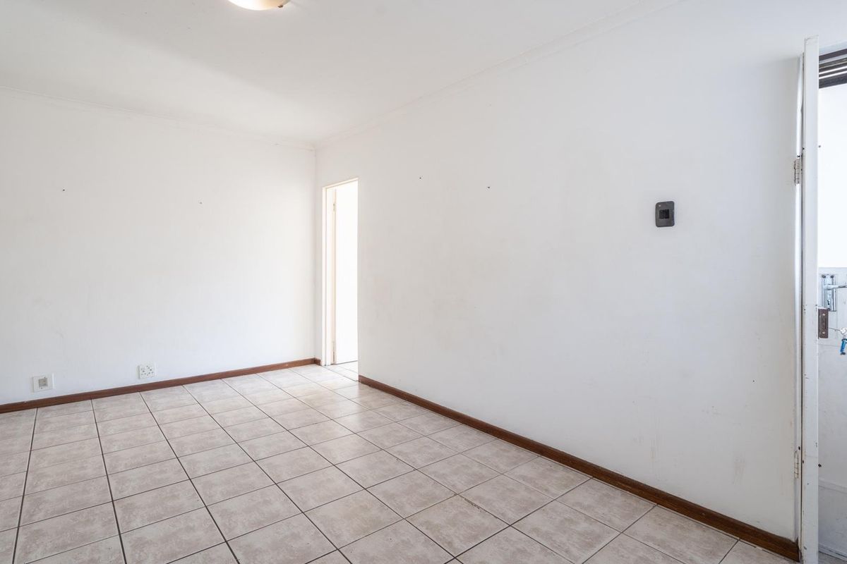 An empty, neutrally painted living area featuring tiled flooring and direct access to an exterior door.