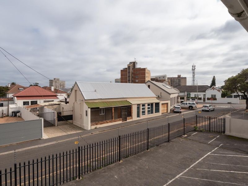 An elevated view overlooking a street, surrounding neighborhood buildings, and a paved parking area secured with metal and electric fencing.