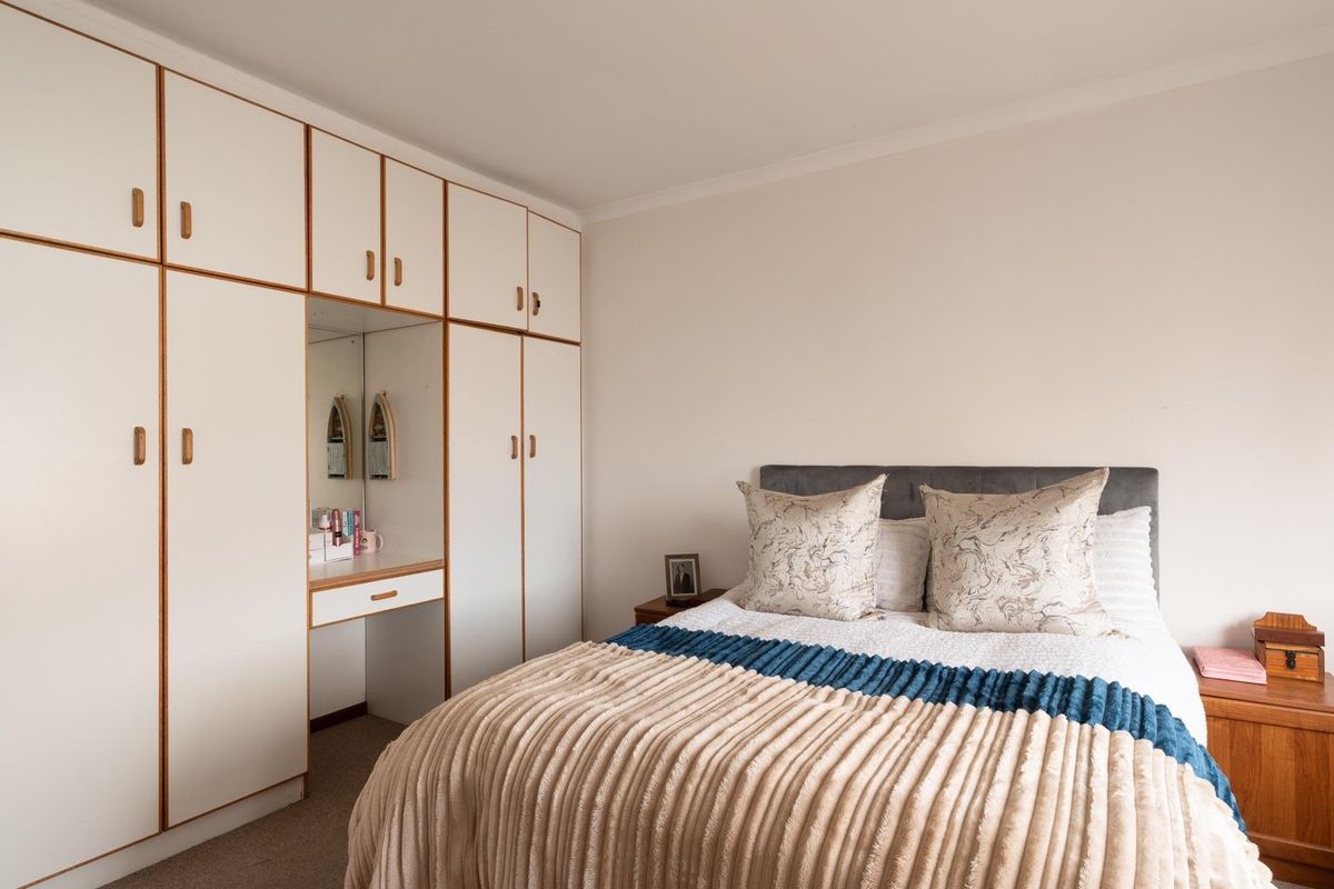 A well-maintained bedroom featuring extensive floor-to-ceiling built-in cupboards with an integrated vanity unit and neutral carpeting.