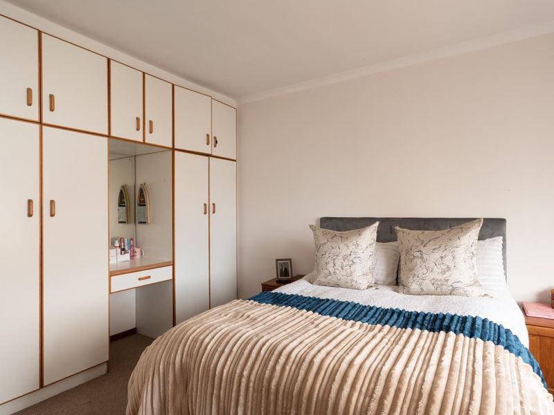 A well-maintained bedroom featuring extensive floor-to-ceiling built-in cupboards with an integrated vanity unit and neutral carpeting.