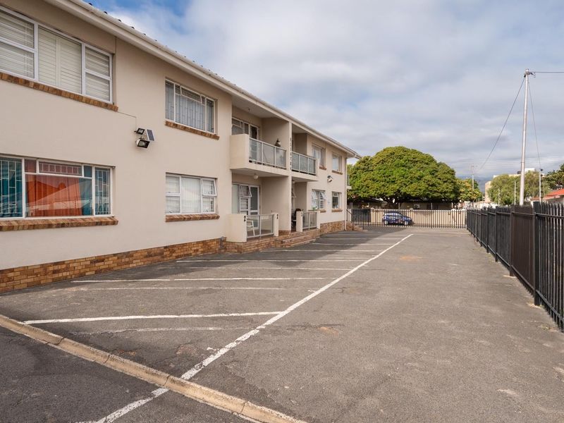 Exterior view of an apartment complex featuring a paved parking area, metal security fencing, and multiple balconies.