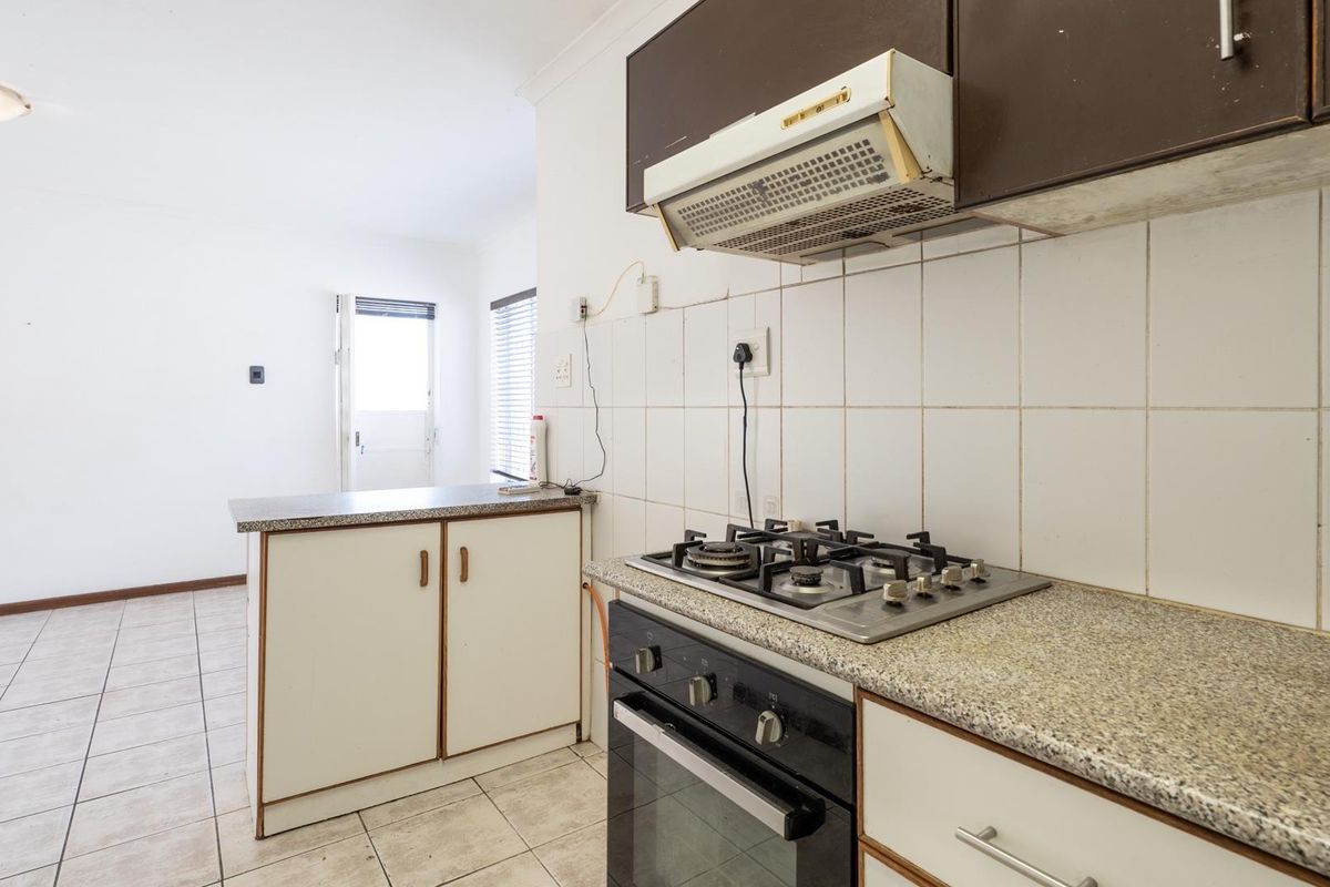 A functional kitchen featuring built-in cabinetry, a gas hob, oven, extractor fan, and tiled flooring, offering a clean and practical layout.