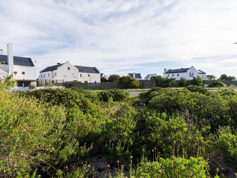 A view of a vacant residential plot featuring native coastal vegetation with established residential homes visible in the background.