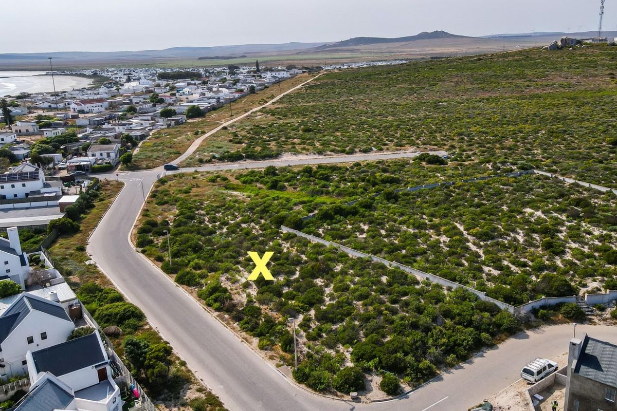 Aerial view of a vacant residential plot situated in a coastal neighborhood with established road access and surrounding infrastructure.