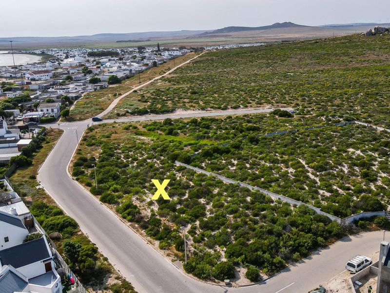 Aerial view of a vacant residential plot situated in a coastal neighborhood with established road access and surrounding infrastructure.