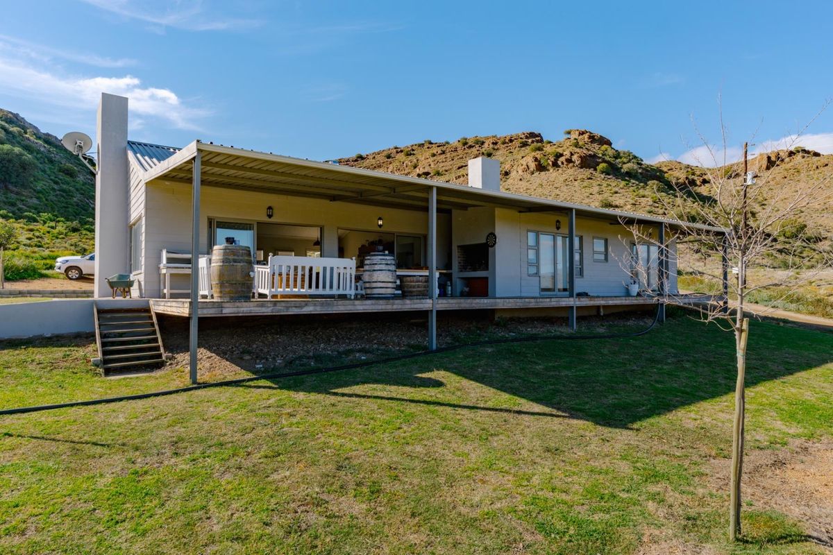 Rear view of the farmhouse featuring a spacious covered timber deck, built-in braai area, and large sliding doors opening to the landscape.