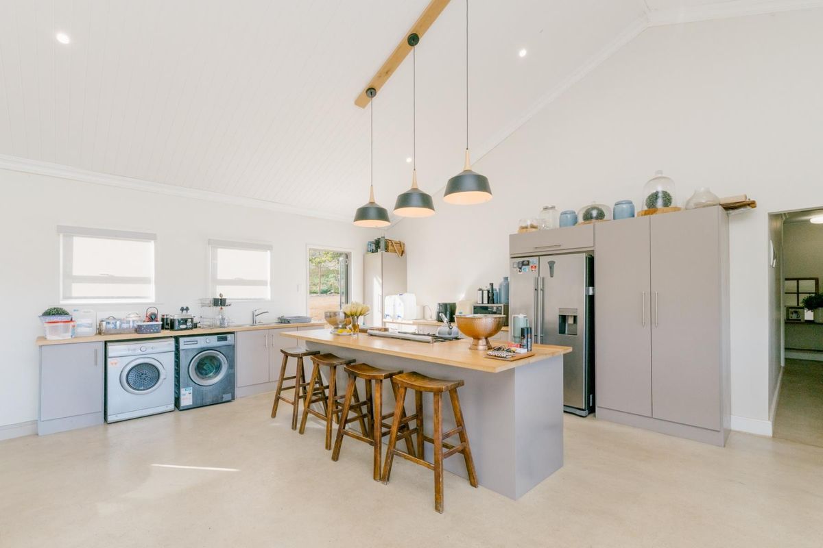 Modern open-plan kitchen featuring a central timber-topped island, sleek cabinetry, vaulted ceilings, and integrated laundry facilities in a bright, well-maintained space.