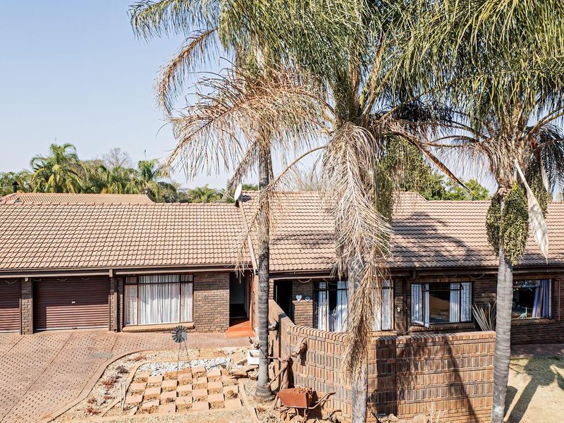 Front elevation of a single-story brick house featuring a tiled roof, double garage, and paved driveway with established garden landscaping.