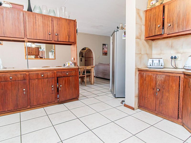 A dated kitchen featuring wooden cabinetry, tiled flooring, and a tiled backsplash, with an open-plan layout leading into the adjacent living area.