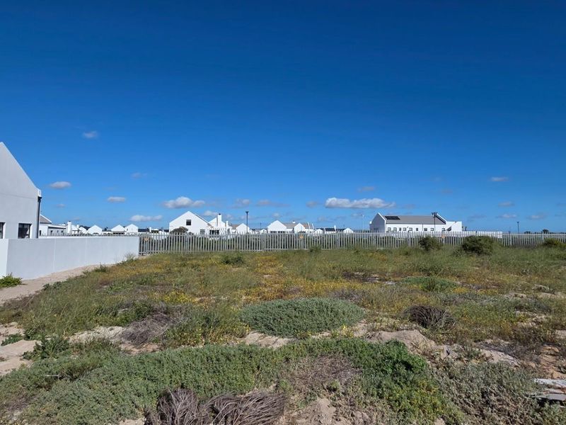 A vacant residential plot featuring natural vegetation, perimeter fencing, and views of neighboring properties in a developed estate setting.