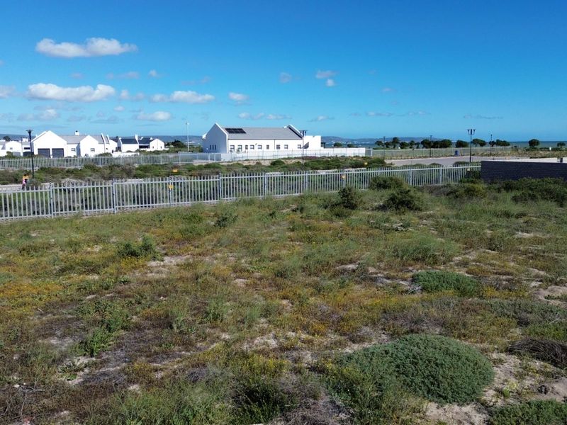 A vacant residential plot featuring natural vegetation, enclosed by perimeter fencing and a boundary wall in a developed coastal estate setting.