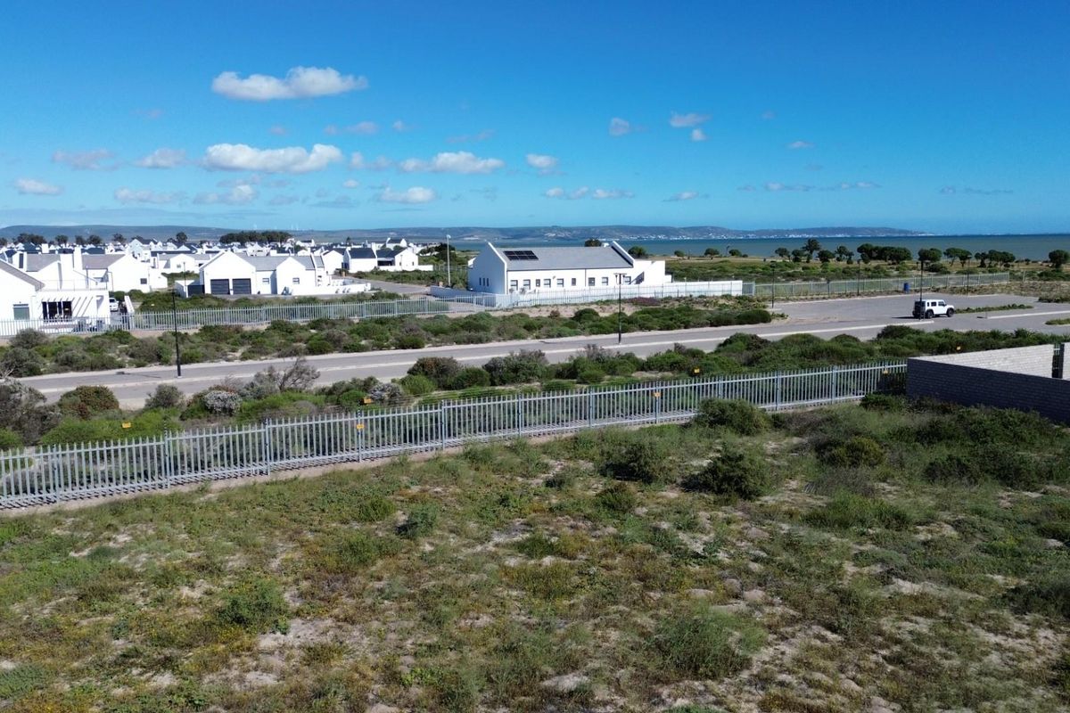 Aerial view of a vacant residential plot featuring perimeter fencing, situated in a coastal neighborhood with nearby road access and surrounding residential properties.