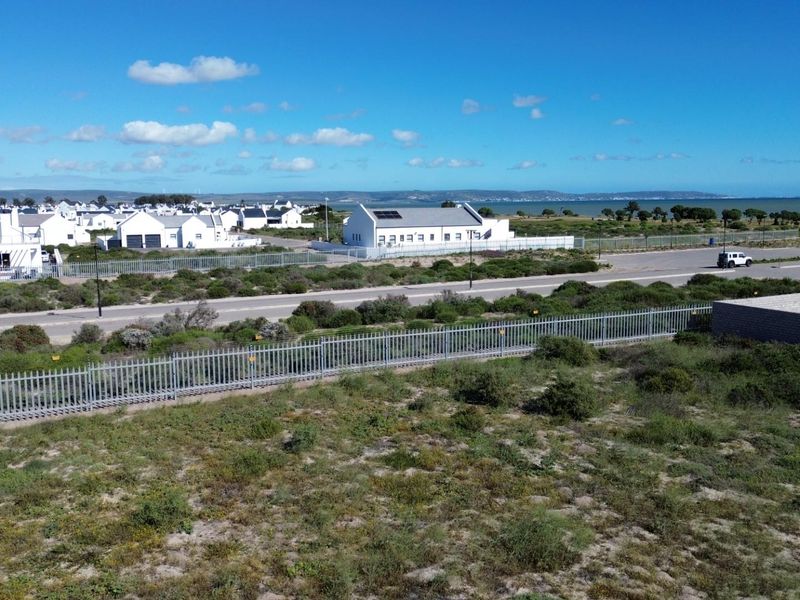 Aerial view of a vacant residential plot featuring perimeter fencing, situated in a coastal neighborhood with nearby road access and surrounding residential properties.