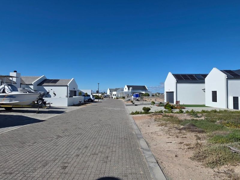 A street view of a residential estate featuring modern white homes with pitched roofs, paved roads, and solar panel installations.