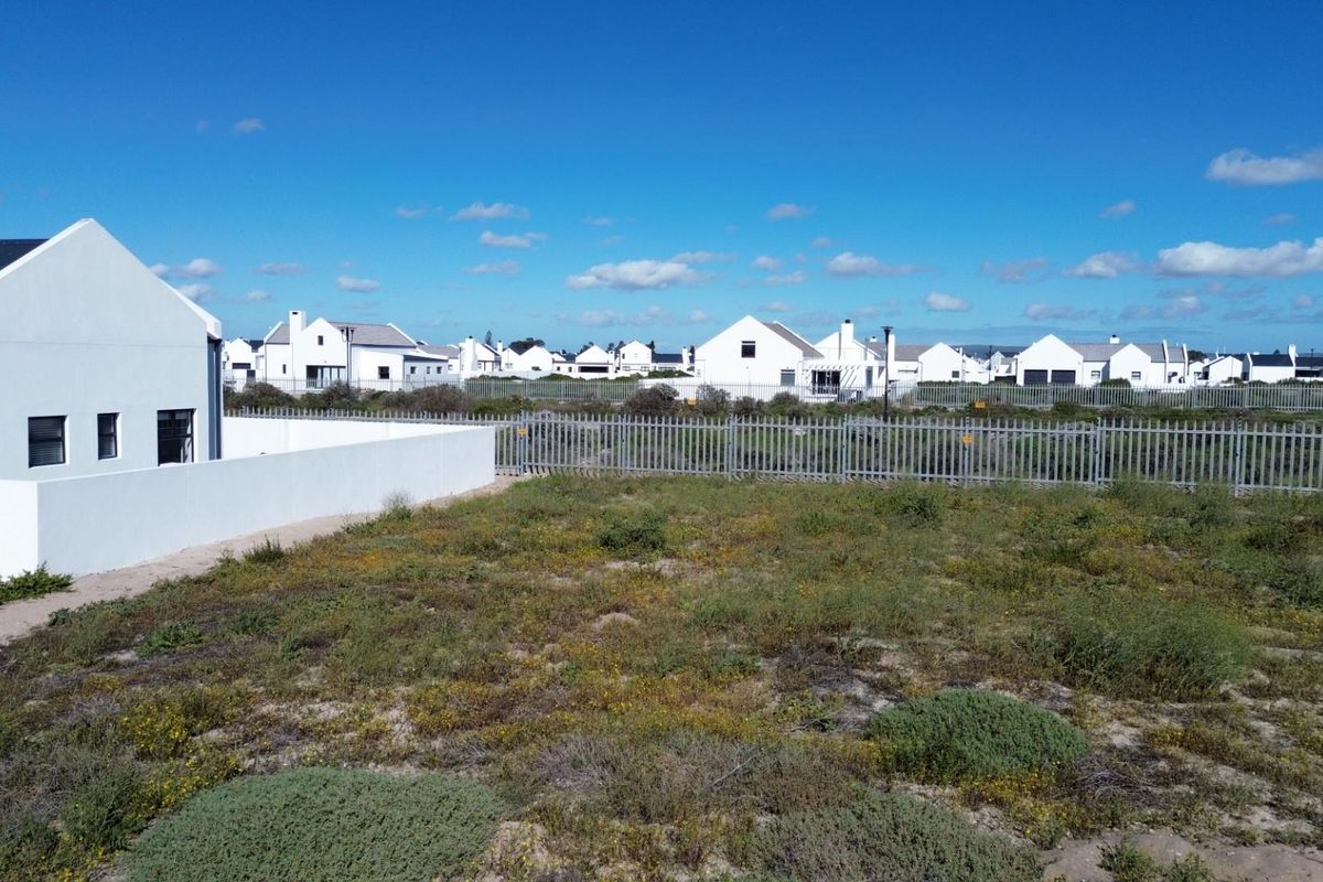A vacant residential plot featuring natural vegetation, enclosed by perimeter fencing and a boundary wall within a developed estate.