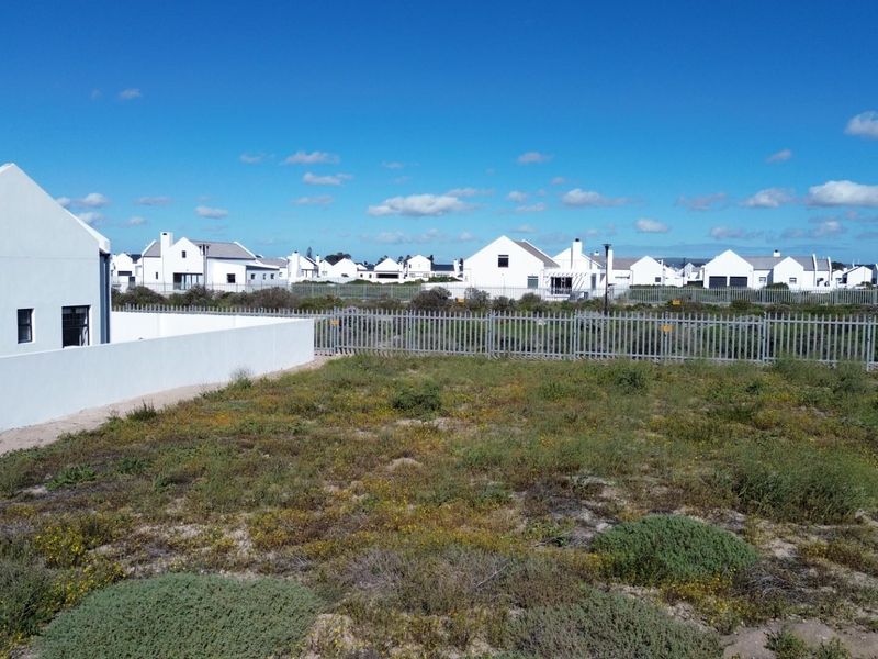 A vacant residential plot featuring natural vegetation, enclosed by perimeter fencing and a boundary wall within a developed estate.