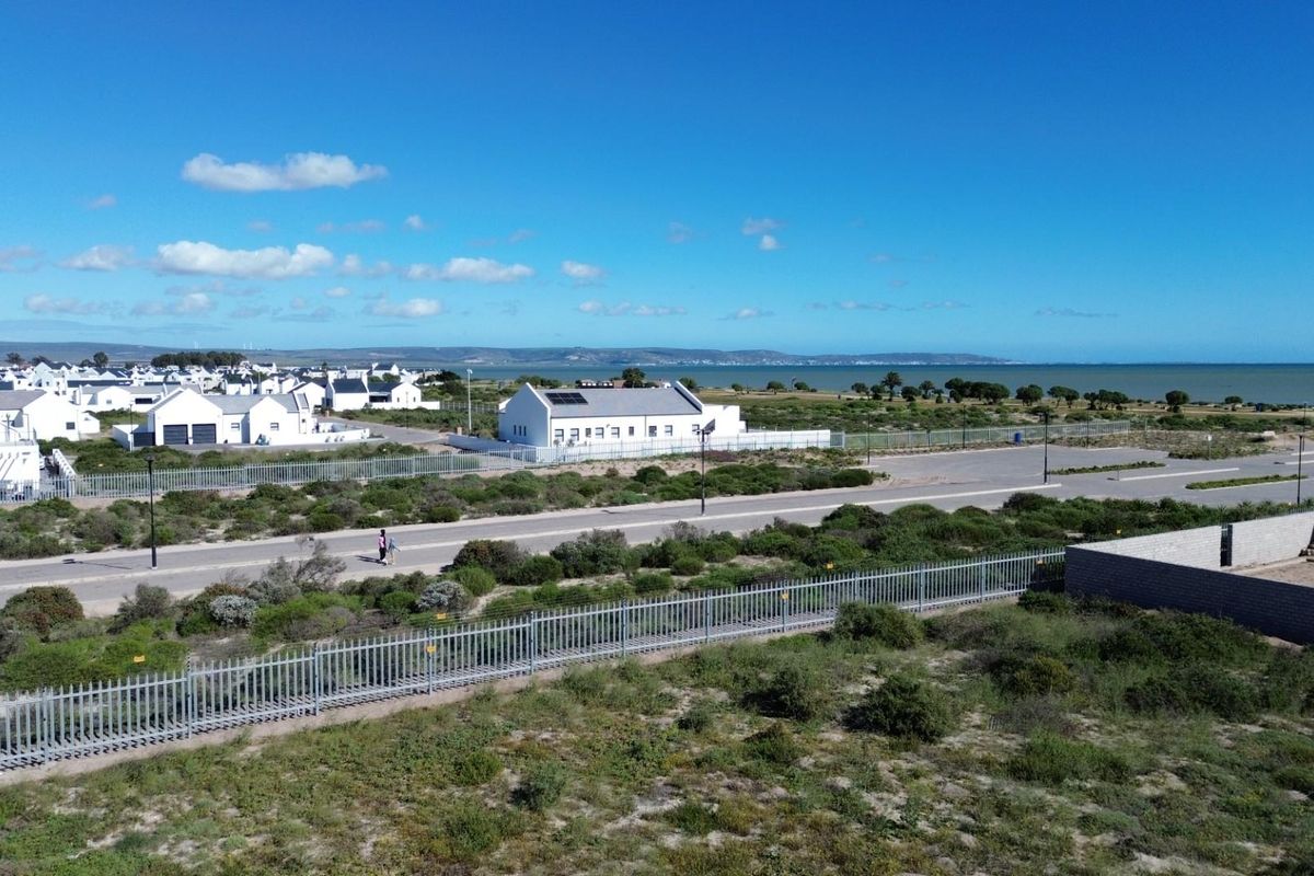 Aerial view of a residential vacant land plot featuring perimeter fencing, adjacent paved roads, and scenic coastal views in a developed estate setting.