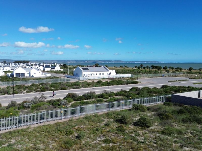 Aerial view of a residential vacant land plot featuring perimeter fencing, adjacent paved roads, and scenic coastal views in a developed estate setting.