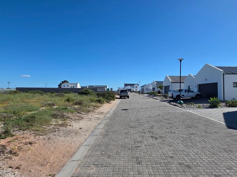A view of a residential street featuring a paved driveway and adjacent vacant land in a modern estate setting.