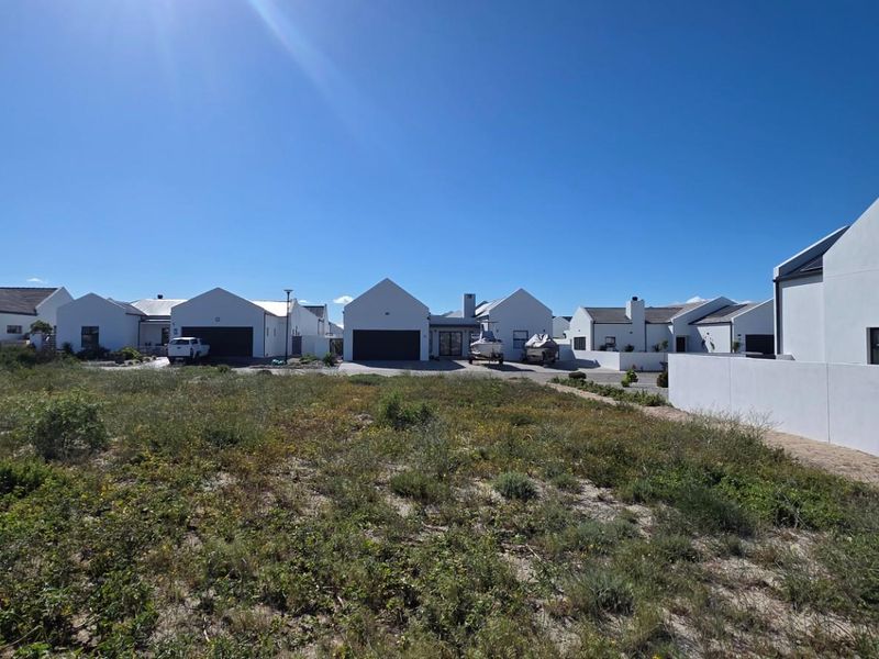 A view of a vacant residential plot situated in a developed estate, featuring surrounding modern homes and established boundary walls.