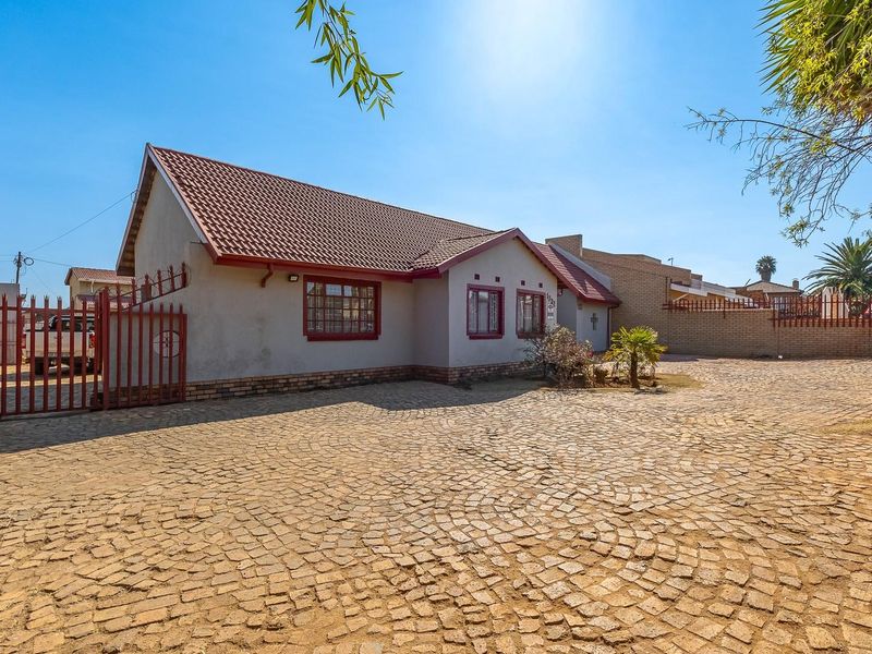 Front exterior view of a single-story house featuring a large cobblestone driveway, tiled roof, and secure metal gate access.